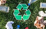 A recycling arrow symbol on green grass with recycling items laying around the symbol