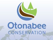 Otonabee Conservation logo: green tree, with a brown strip, and then a blue strip below it and the words "Otonabee Conservation" in blue under that.
