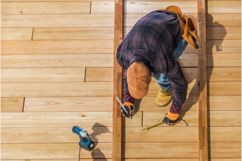 A man working on a deck with tools in-hand and beside him.