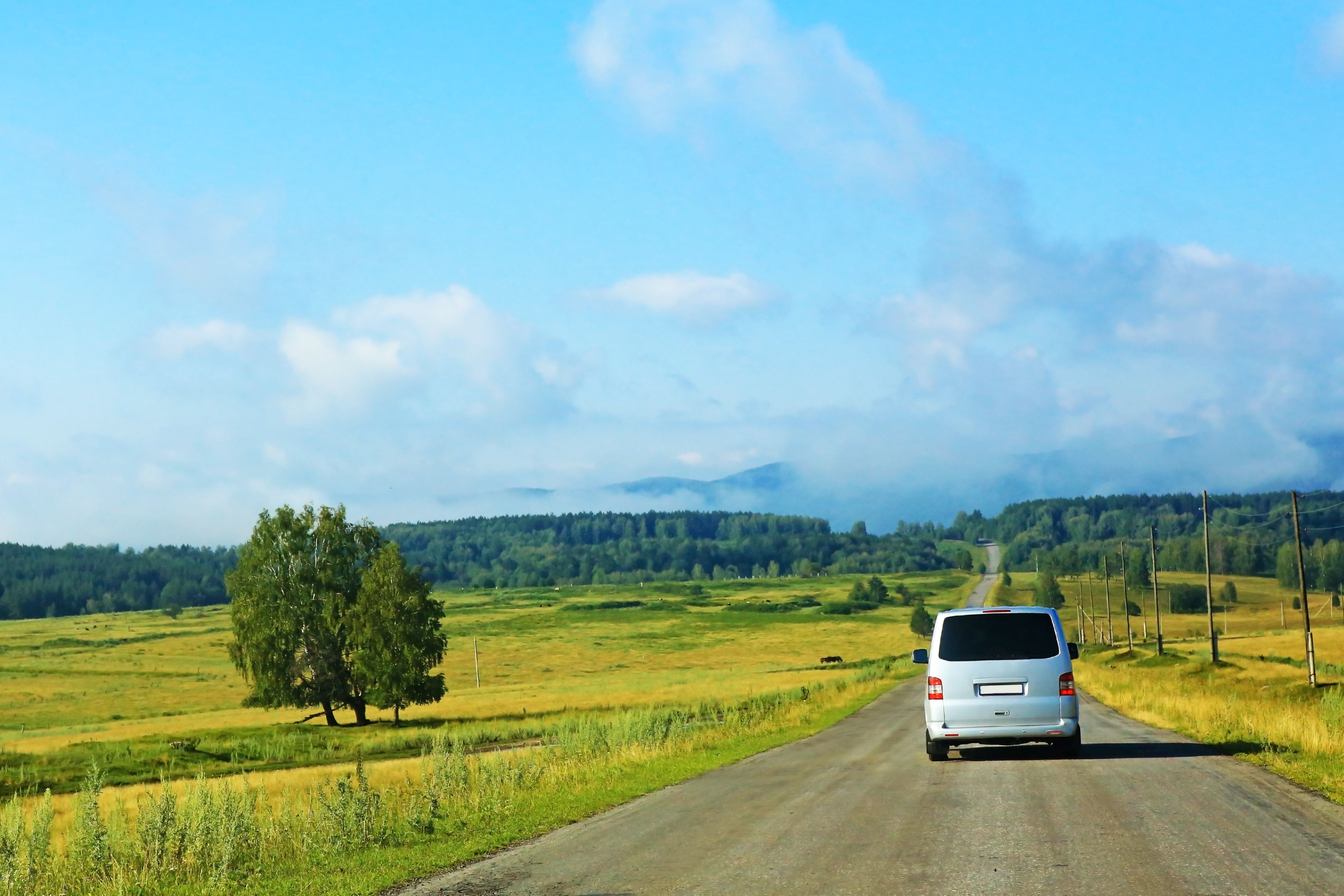 Rural setting with a road and a van driving on the road.