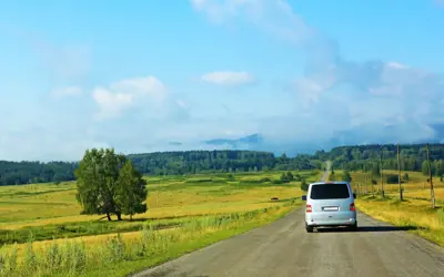 Rural setting with a road and a van driving on the road.