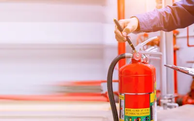 A fire extinguisher being checked by a hand with a clipboard