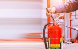 A fire extinguisher being checked by a hand with a clipboard