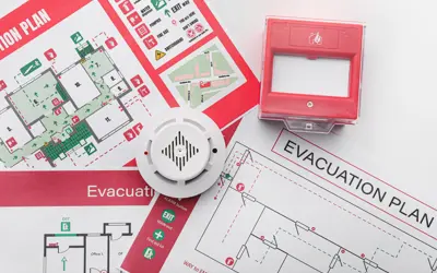 Paper copies of escape plans on a table, with a smoke alarm and a pull station sitting on top