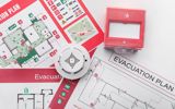 Paper copies of escape plans on a table, with a smoke alarm and a pull station sitting on top