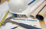 A building permit on a table, with building plans, tools and a hard hat sitting on top