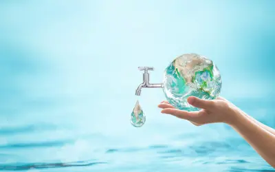 Blue water background with a hand holding a globe of water, with a tap attached and a drop coming out ot the tap.