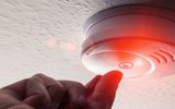 A hand push the smoke alarm button with a red light indicator showing.